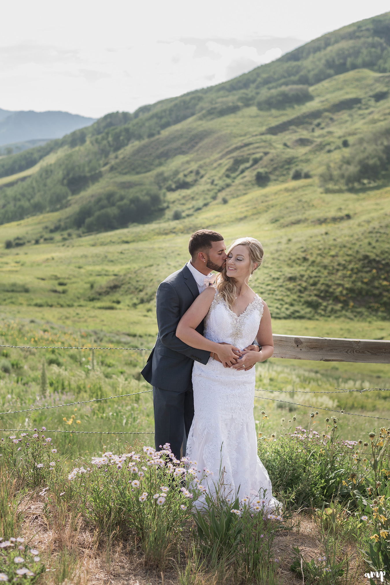 Bride and groom sharing a kiss among the wildflowers with mountains in the distance
