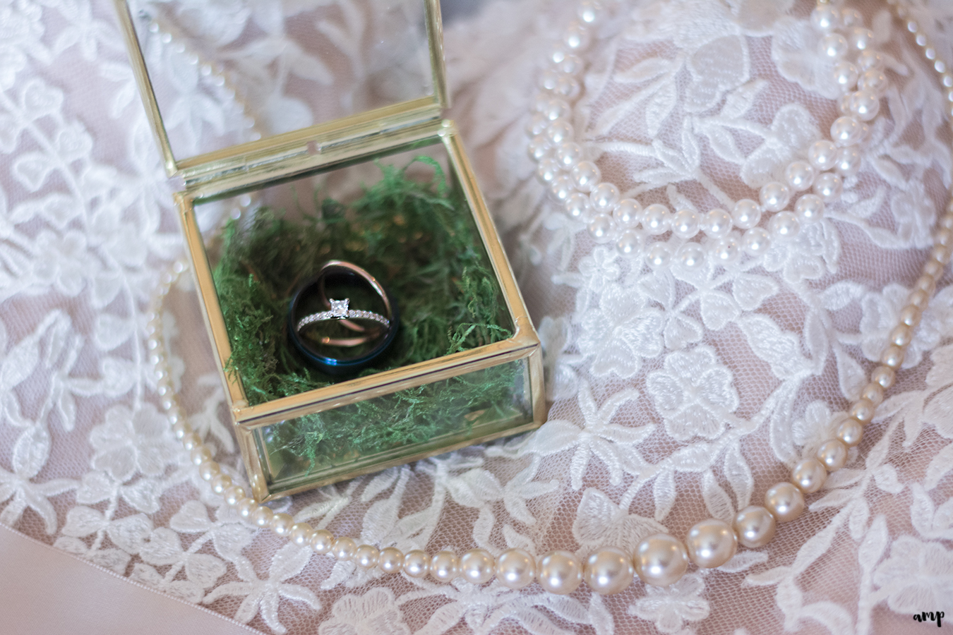 Wedding rings in antique gold and glass ring box atop lacy wedding dress and pearls